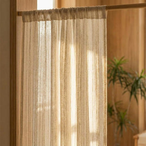 Gros plan sur un rideau en gaze rayé beige suspendu à une tringle en bois, lumière tamisée