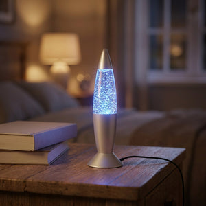 Lampe à lave USB argentée allumée en bleu posée sur une table de nuit en bois