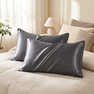 Deux taies d'oreiller en satin gris posées sur un lit dans une chambre lumineuse