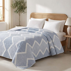 Jeté de lit réversible à chevrons bleus posé sur un lit dans une chambre méditerranéenne lumineuse