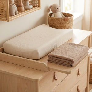 Housse de matelas à langer en gaze de coton posée sur un plan à langer dans une chambre de bébé lumineuse