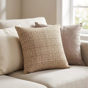 Housse de coussin beige tissée posée sur un canapé en lin dans un salon lumineux