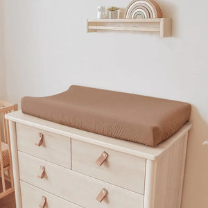 Housse de matelas à langer taupe posée sur une commode à langer en bois clair