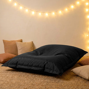 Housse de pouf géant noire posée sur un tapis en jute avec guirlande lumineuse