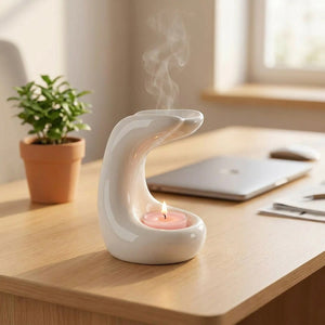Brûle-parfum en céramique blanche allumé sur un bureau à côté d'une plante verte