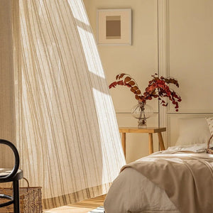 Rideau en gaze rayé beige suspendu devant une fenêtre baignée de lumière dans une chambre