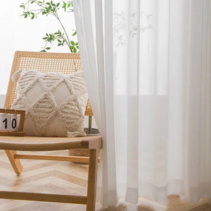 Voilage en tulle blanc suspendu près d'un fauteuil en rotin avec coussin