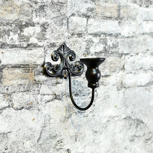 Bougeoir mural en métal noir de style baroque vu de face sur un mur
