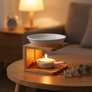 Brûle-parfum en céramique blanche et bambou avec bougie allumée posé sur une table en bois