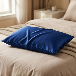 Taie d'oreiller en soie bleu foncé posée sur un lit avec couverture tricotée