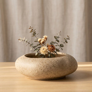 Vase galet en céramique beige avec composition florale séchée sur une table en bois