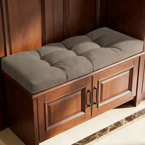 Coussin banquette en lin au style intemporel, capitonné et de teinte neutre, posé sur un meuble en bois foncé avec portes et poignées noires, dans une ambiance chaleureuse et élégante.