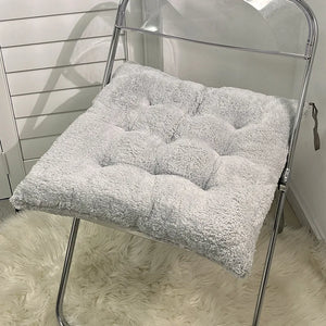 Coussin d’assise carré épais moelleux avec surface capitonnée et texture douce, posé sur une chaise pliante en métal pour offrir un confort enveloppant.