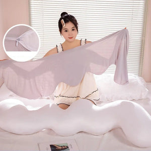 Un long coussin de lit ondulé blanc posé sur un lit, avec une forme sinueuse et moelleuse, tenu par une personne montrant sa souplesse et son aspect confortable.