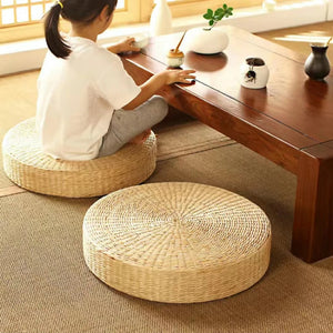 Coussin de sol en paille style japonais, rond et tressé, placé sur un tapis beige devant une table basse en bois, créant une ambiance zen et naturelle.