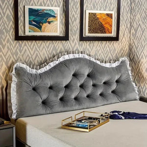 Coussin tête de lit capitonné confortable avec boutons décoratifs et bordure volantée, installé contre un mur avec tableaux encadrés au-dessus du lit.