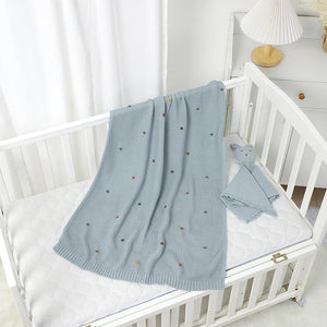 Une couverture bébé crochet à pois délicatement posée sur un berceau blanc, avec une texture tricotée douce et un rendu apaisant, idéale pour un univers enfantin chaleureux.