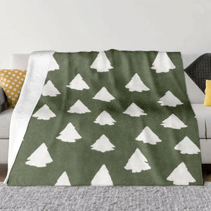 Un grand plaid à motifs sapins double-face étendu sur un canapé, avec des formes de sapins répétées et une texture douce, créant une ambiance chaleureuse et hivernale.