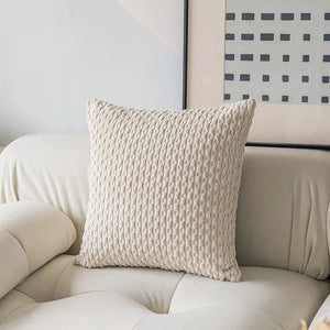 Gros coussin doux style Boho de couleur écrue avec texture en relief, posé sur un canapé beige clair dans un salon lumineux aux lignes épurées.