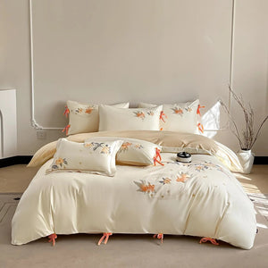 Une parure de lit chic à motifs floraux brodés sur fond crème avec petits liens décoratifs, disposée dans une chambre minimaliste et lumineuse.