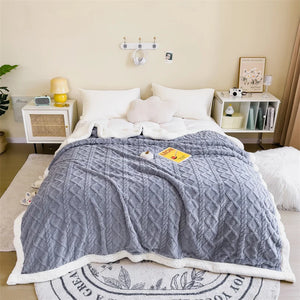 Une parure de lit cocooning double face épaisse et texturée posée sur un lit blanc, avec un côté doux effet laine visible à l’intérieur et une surface extérieure à motif relief.