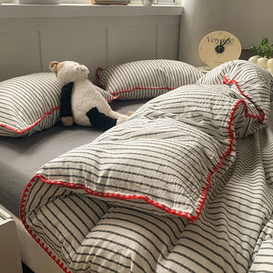 Une parure de lit style minimaliste avec fines rayures et finitions contrastées, accompagnée de taies assorties, disposée dans une chambre lumineuse à l’ambiance épurée.