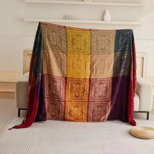 Plaid canapé style bohème avec assemblage de motifs floraux et ornementaux en patchwork, tenu déployé devant un canapé dans un intérieur lumineux.