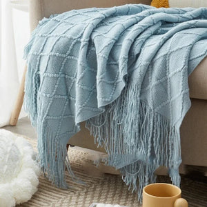 Un plaid canapé tricot texturé style nordique avec motif en relief et franges, délicatement posé sur un canapé, créant une ambiance cosy et élégante.