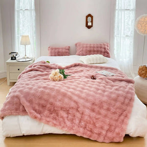 Un plaid chaud doux et cocooning à texture gaufrée disposé sur un lit avec des coussins assortis, créant une atmosphère confortable et apaisante dans une chambre lumineuse.