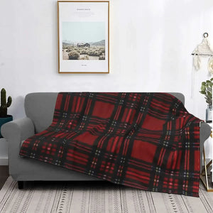 Un plaid tartan traditionnel à carreaux délicatement posé sur un canapé gris dans un salon lumineux, apportant une touche chaleureuse et classique à l’espace.