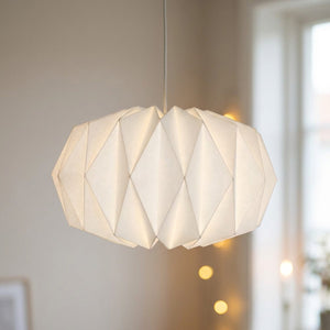 Abat-jour origami en papier blanc forme citrouille aplatie suspendu dans un salon clair