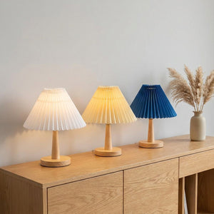 Trois abat-jours plissés de style japonais en blanc jaune et bleu sur console en bois style Japandi