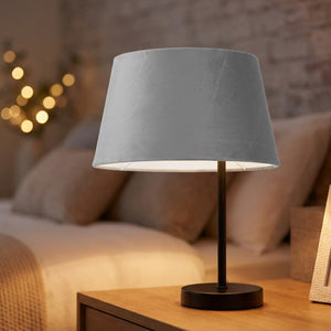 Abat-jour conique en velours gris posé sur une lampe de chevet allumée dans une chambre chaleureuse