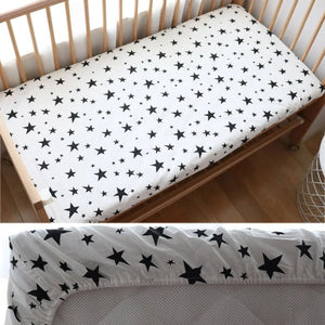 Drap housse bébé motif étoiles noires installé sur un matelas de berceau en bois