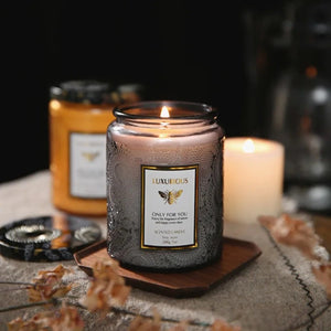 Bougie parfumée en pot embossé gris avec flamme allumée sur plateau en bois et fleurs séchées