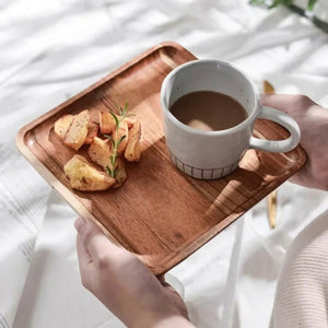 Plateau bois acacia tenu en main avec tasse de café et collation