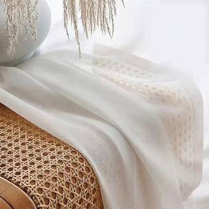 Détail du tissu voile blanc posé sur un banc en rotin