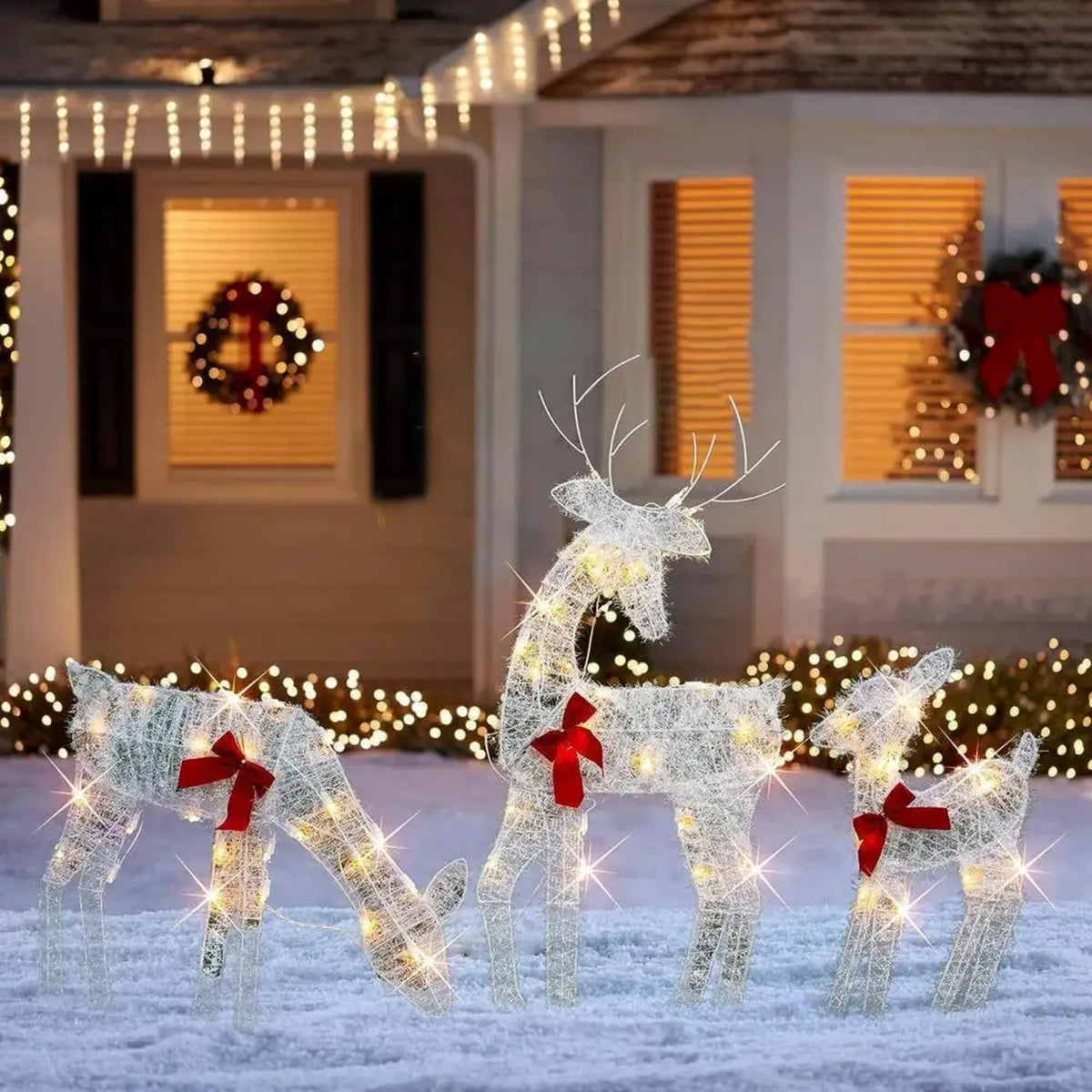 Famille de 3 rennes lumineux devant une maison décorée pour Noël