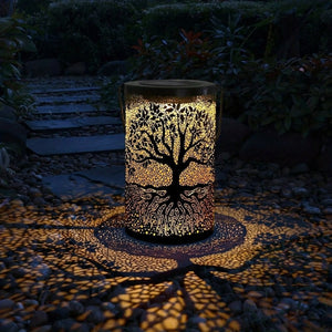 Lanterne solaire arbre de vie allumée posée sur une allée de jardin la nuit