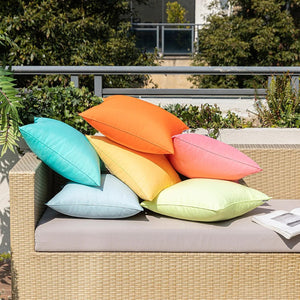 Housses de coussin extérieur turquoise et jaune posées au sol devant un canapé en rotin