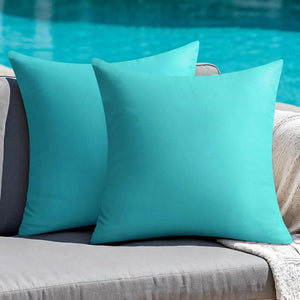 Housses de coussin extérieur turquoise posées sur un canapé de jardin gris au bord d'une piscine
