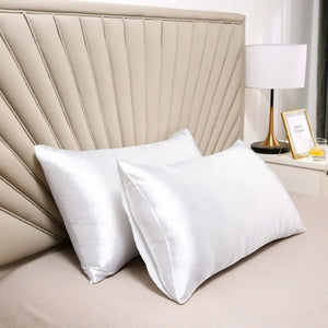 Taies d'oreiller blanches en satin posées sur un lit avec tête de lit capitonnée