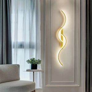 Applique murale LED dorée sur un mur clair à côté d'un fauteuil et d'une plante