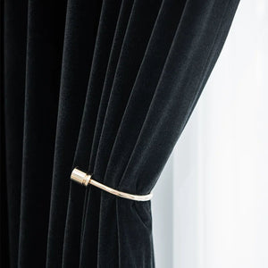 Détail de la texture veloutée du rideau noir avec embrasse dorée