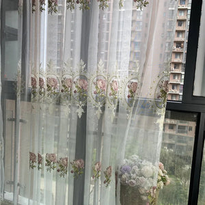 Voilage blanc brodé de pivoines suspendu à une fenêtre laissant passer la lumière