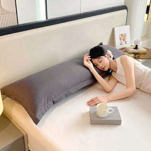 Taie de traversin gris foncé sur un lit avec tête de lit capitonnée