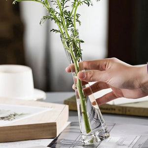 Vase soliflore en verre à bouche inclinée tenu en main avec du feuillage