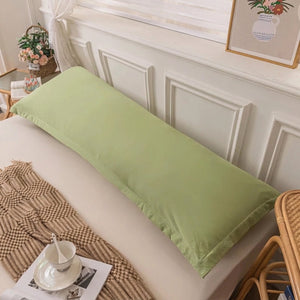 Taie de traversin vert sauge posée sur un lit avec une personne qui la câline