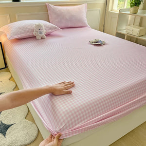 Drap-housse à carreaux rose posé sur un lit avec taies assorties