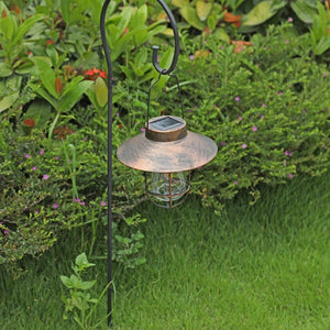Lanterne solaire bronze suspendue à un piquet crochet dans un jardin en journée